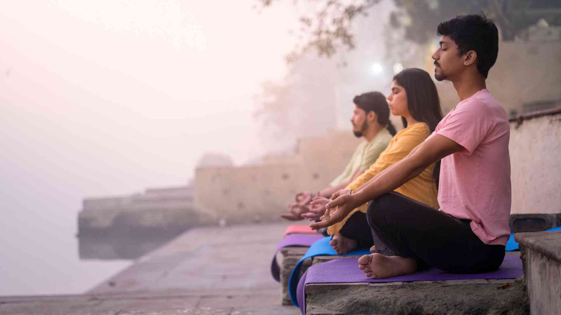 A serene scene of individuals practicing yoga by the Ganges River, surrounded by nature and tranquility.