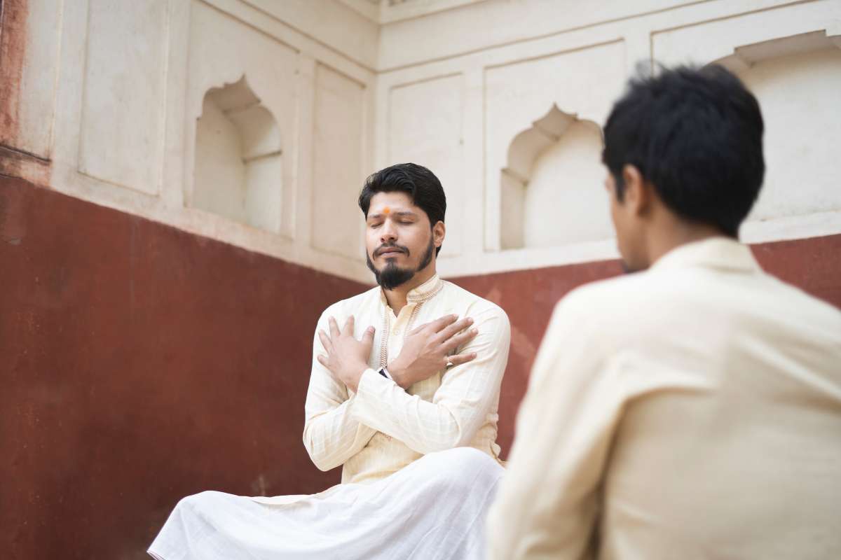 A man sits on the ground with his hands clasped, reflecting in a moment of contemplation and stillness.